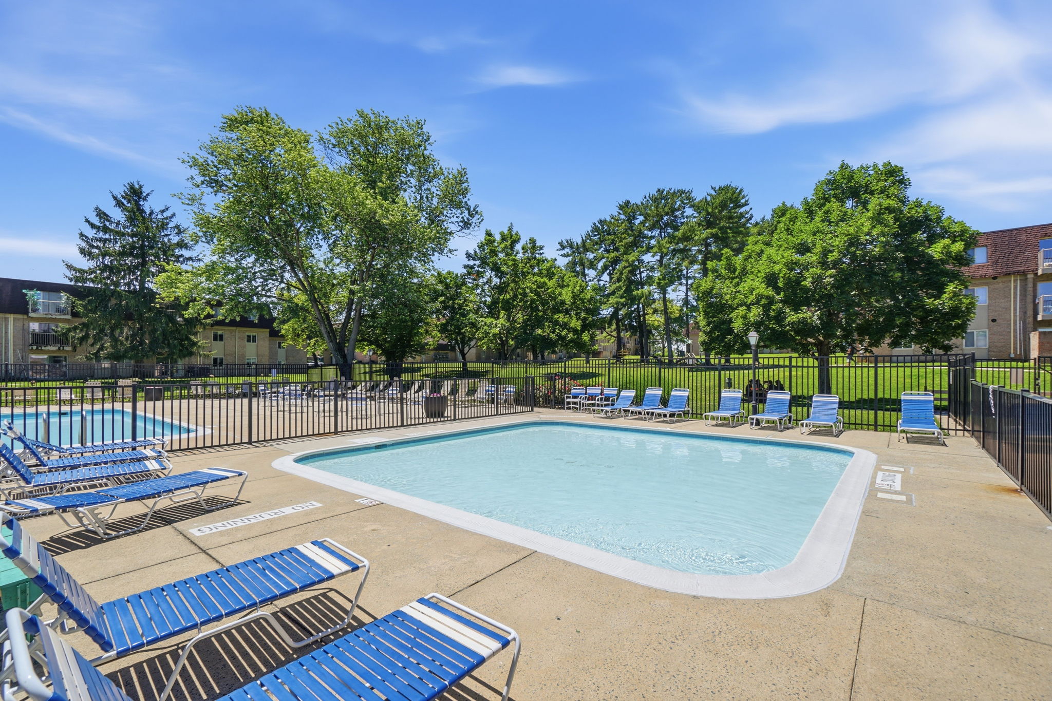 A large outdoor swimming pool surrounded by blue lounge chairs and trees.